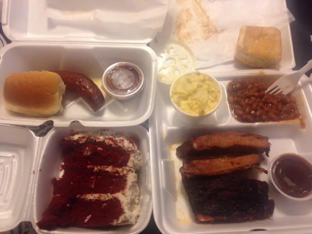 Two BBQ plates with ribs, sausage, red velvet cake and sides